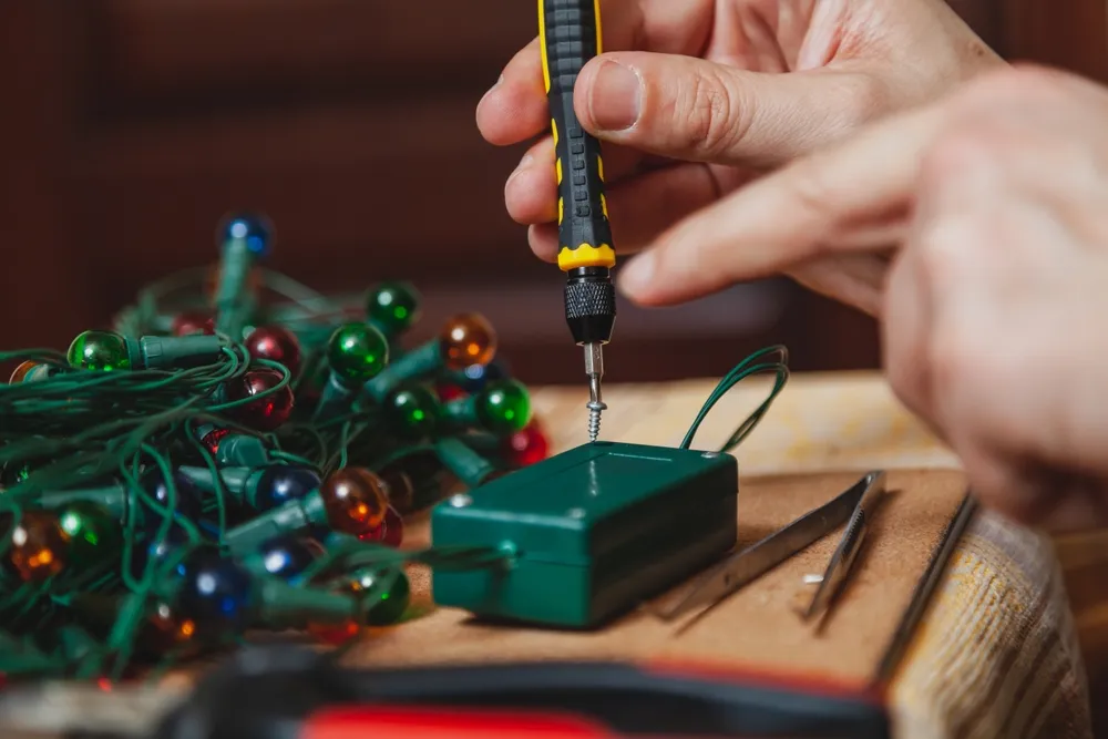 A technician repairing a strand of colored holiday lights on a workbench